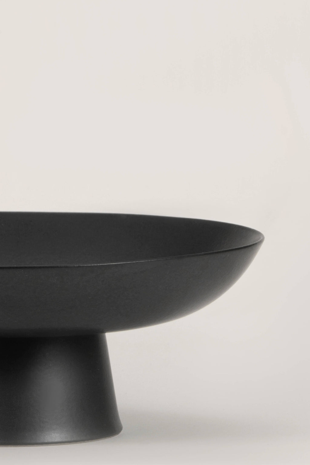 Matte black ceramic footed bowl, ideal for home decor and versatile for various contents like fruits and decorative items.