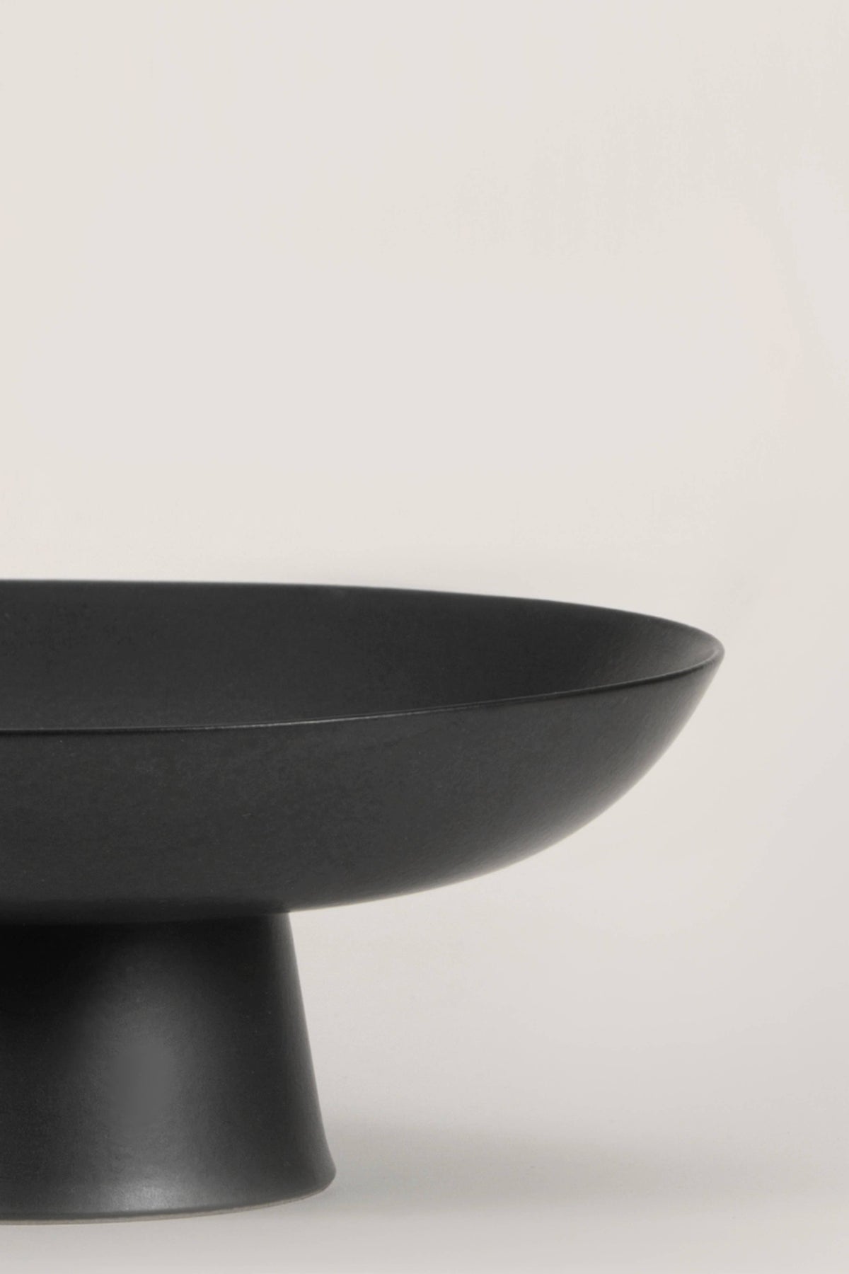 Matte black ceramic footed bowl, ideal for home decor and versatile for various contents like fruits and decorative items.